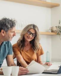 Couple looking at laptop and paperwork while discussing their finances at home