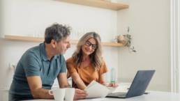 Couple looking at laptop and paperwork while discussing their finances at home