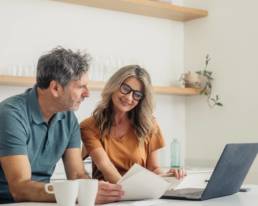 Couple looking at laptop and paperwork while discussing their finances at home