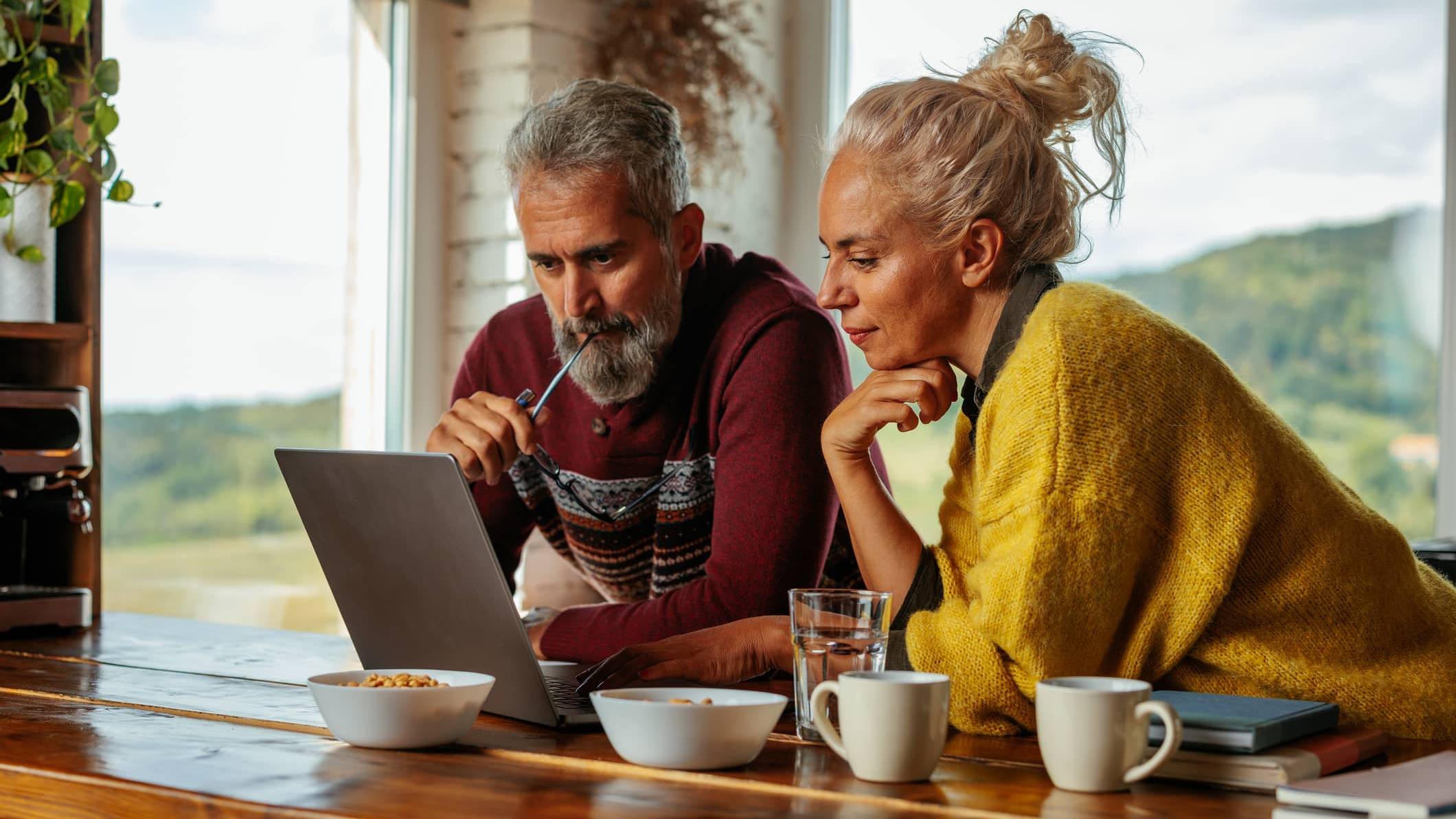 Middle-aged couple looking at a laptop together at home while discussing investment decisions during a market downturn.