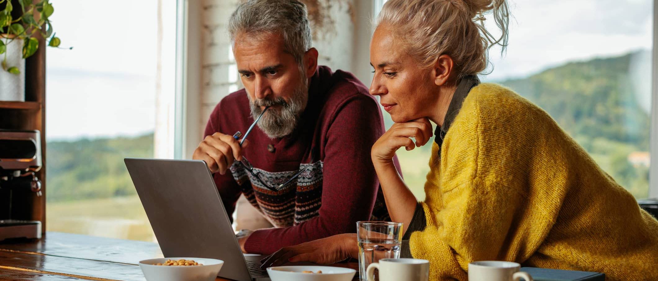 Middle-aged couple looking at a laptop together at home while discussing investment decisions during a market downturn.