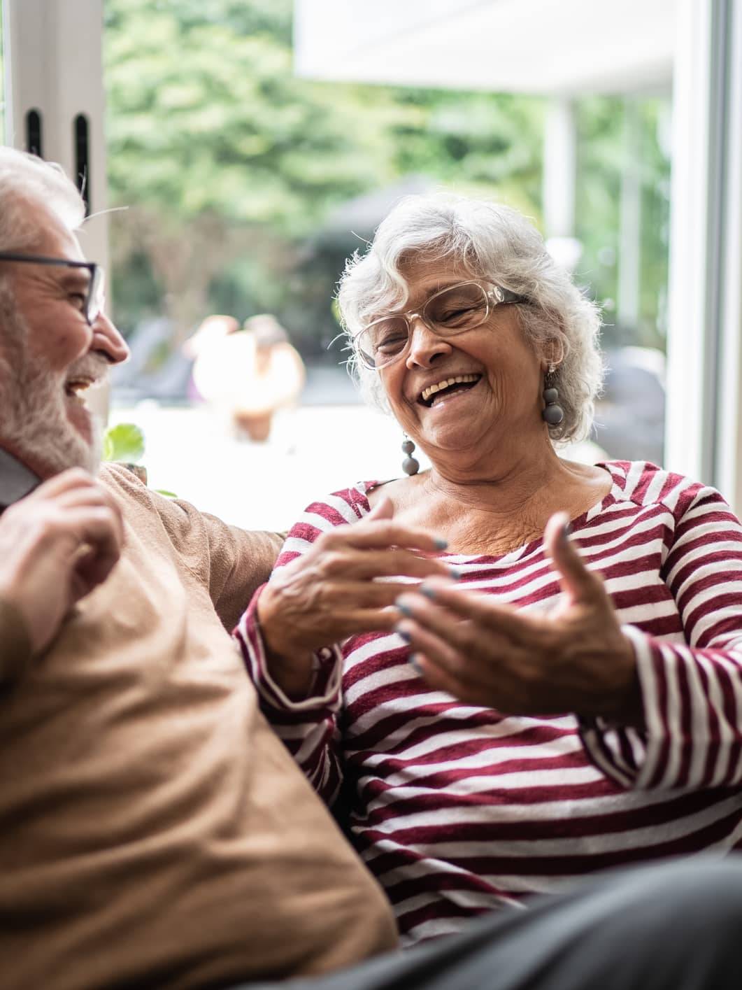 Older couple laughing together on a sofa at home while discussing their future plans