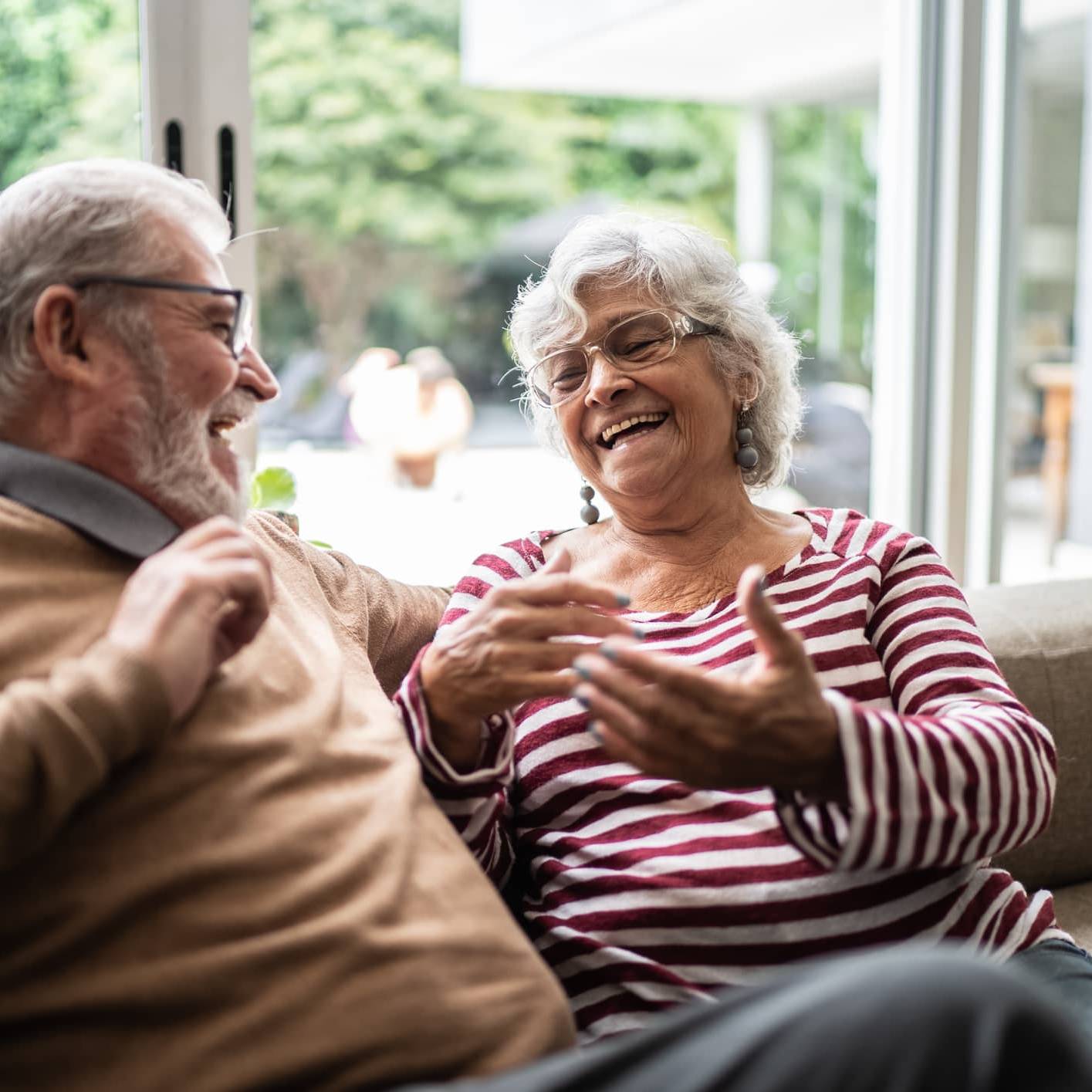 Older couple laughing together on a sofa at home while discussing their future plans