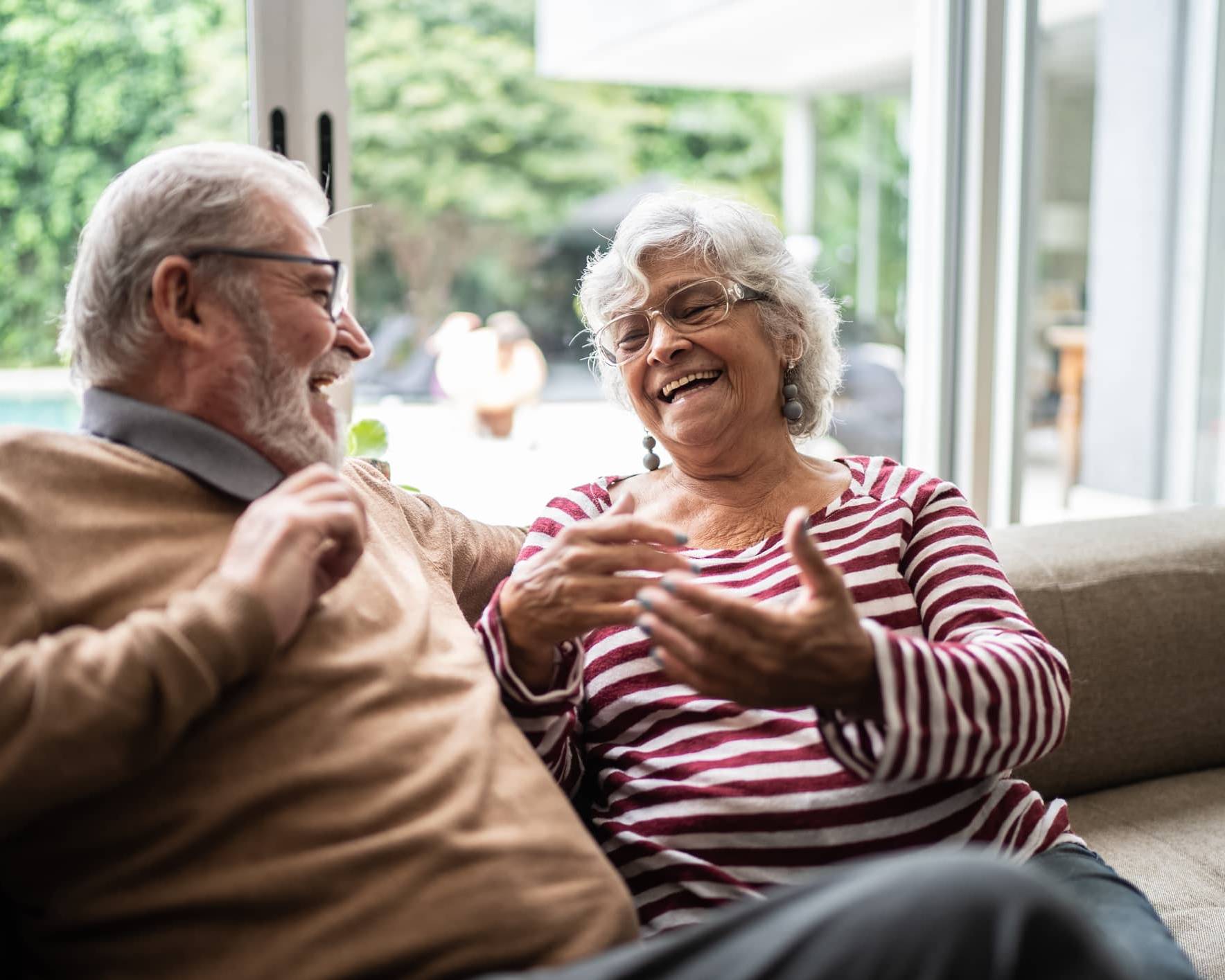 Older couple laughing together on a sofa at home while discussing their future plans