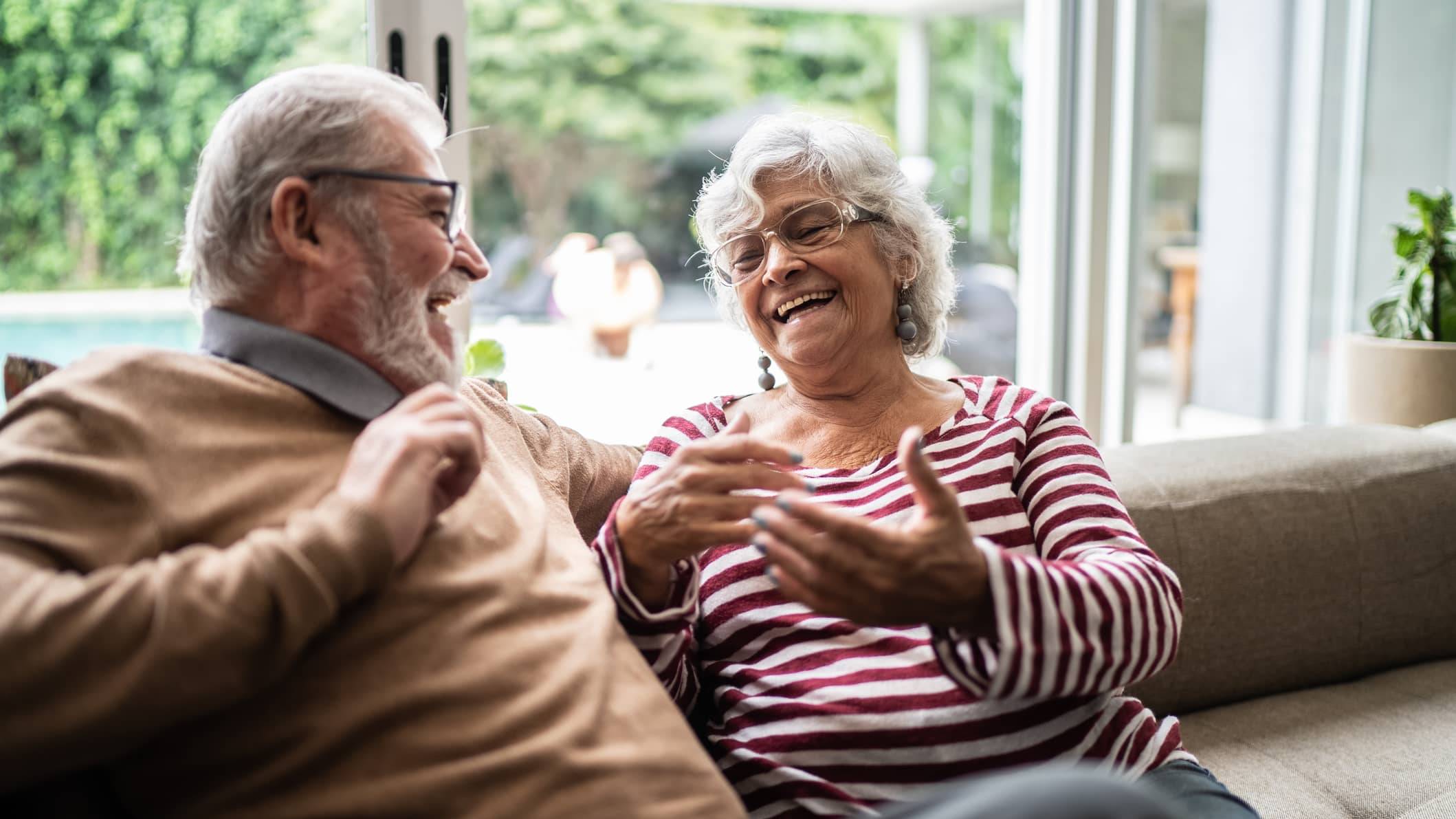 Older couple laughing together on a sofa at home while discussing their future plans