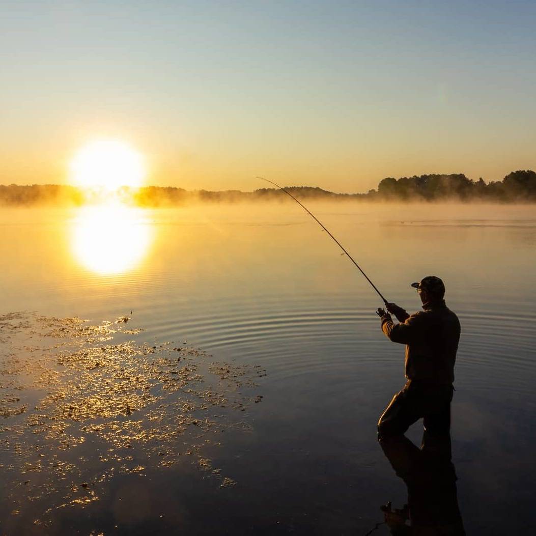 Wide view of a person fishing on a calm lake at sunrise, symbolising long-term business exit planning.
