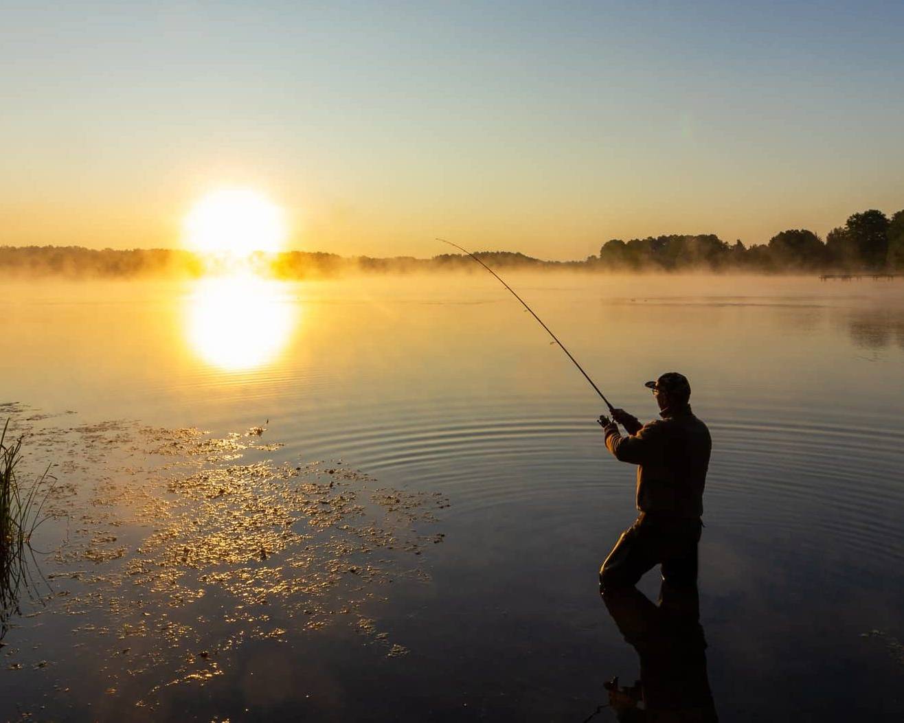 Wide view of a person fishing on a calm lake at sunrise, symbolising long-term business exit planning.