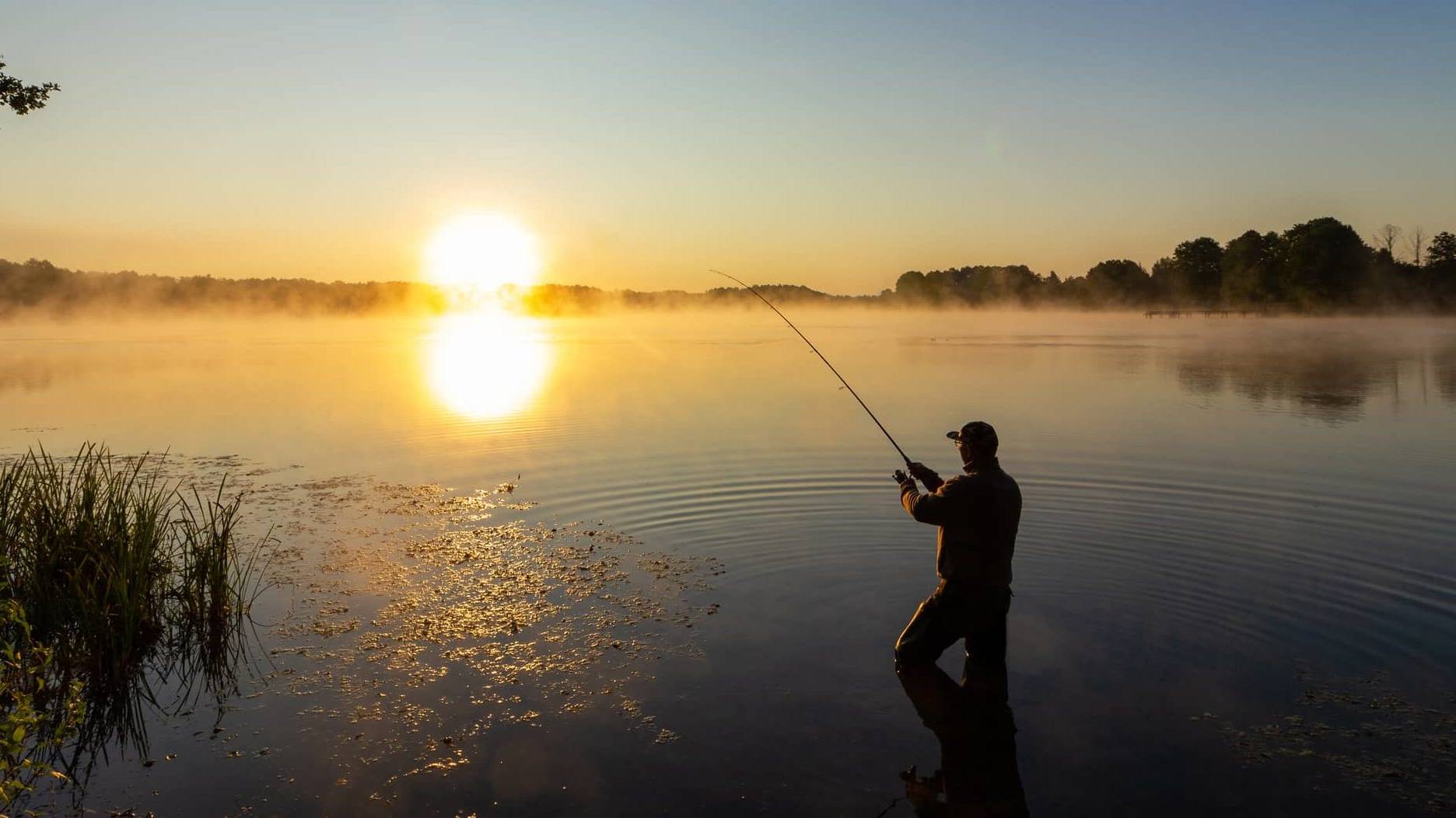 Wide view of a person fishing on a calm lake at sunrise, symbolising long-term business exit planning.