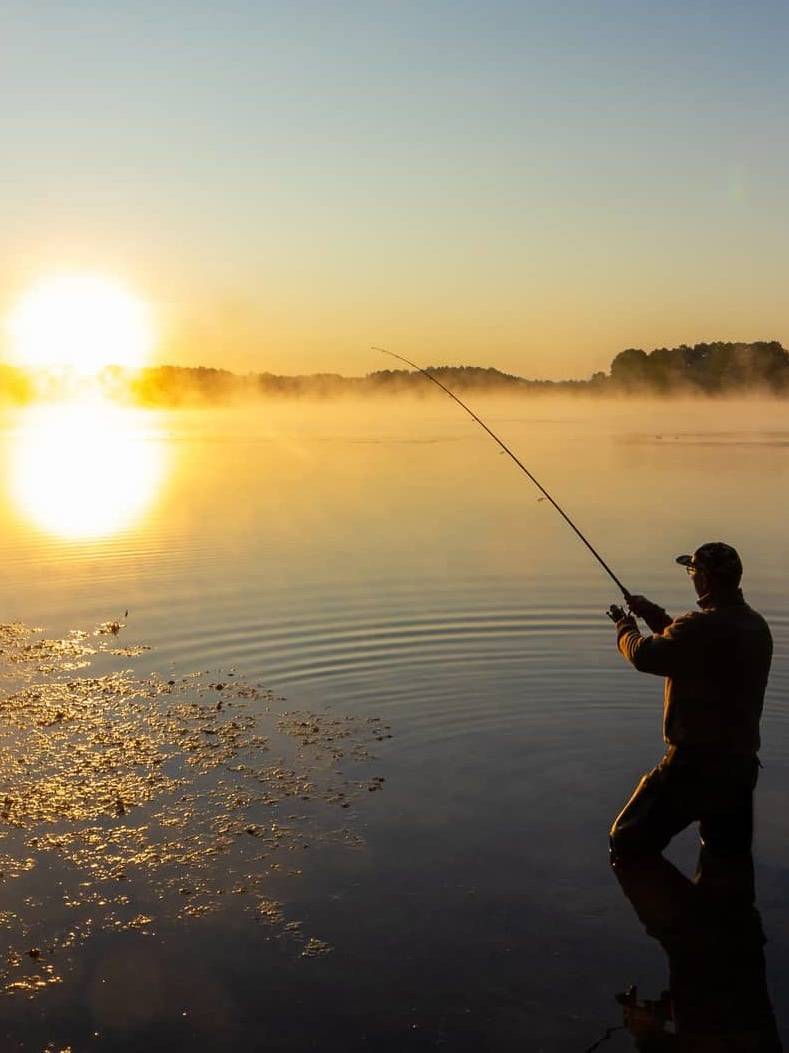 Wide view of a person fishing on a calm lake at sunrise, symbolising long-term business exit planning.