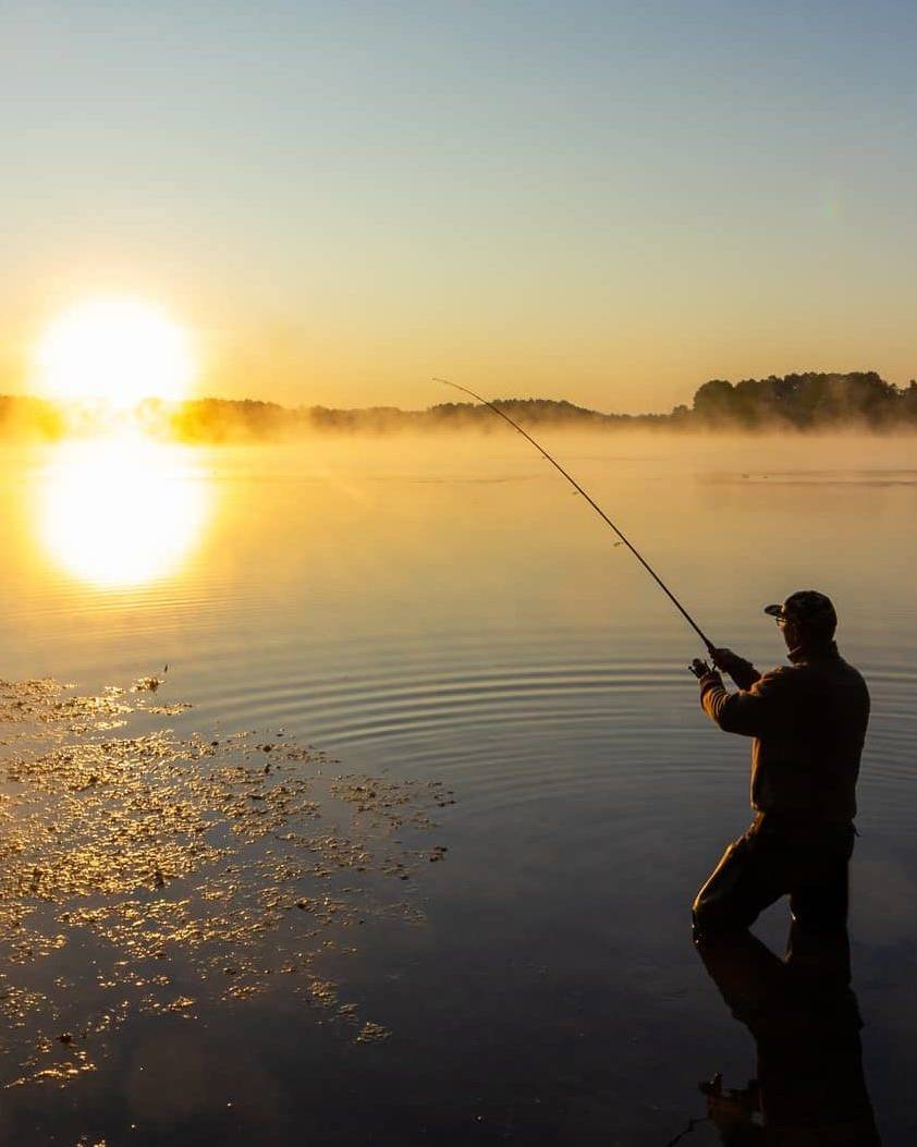 Wide view of a person fishing on a calm lake at sunrise, symbolising long-term business exit planning.