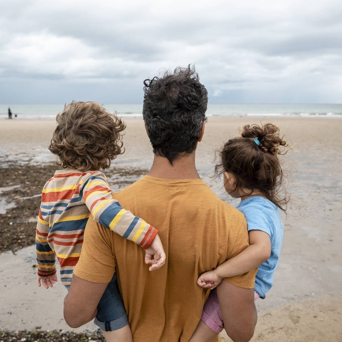 Parent carrying two children while looking out across a beach, symbolising financial security and future planning.