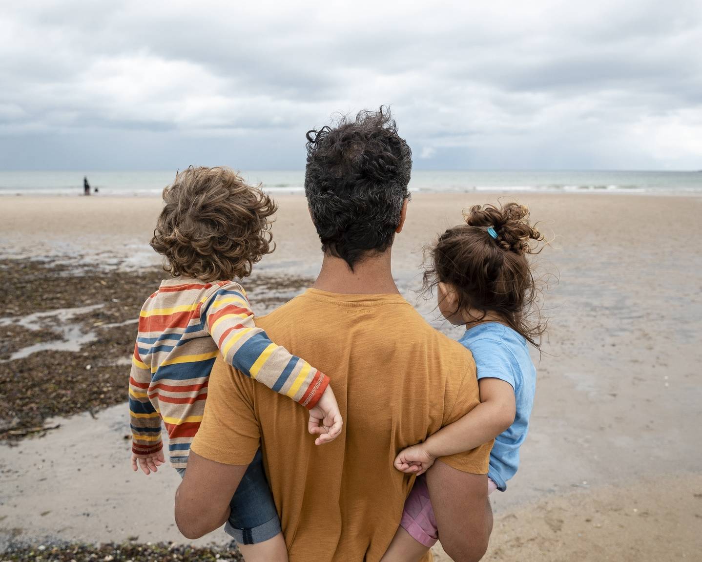 Parent carrying two children while looking out across a beach, symbolising financial security and future planning.