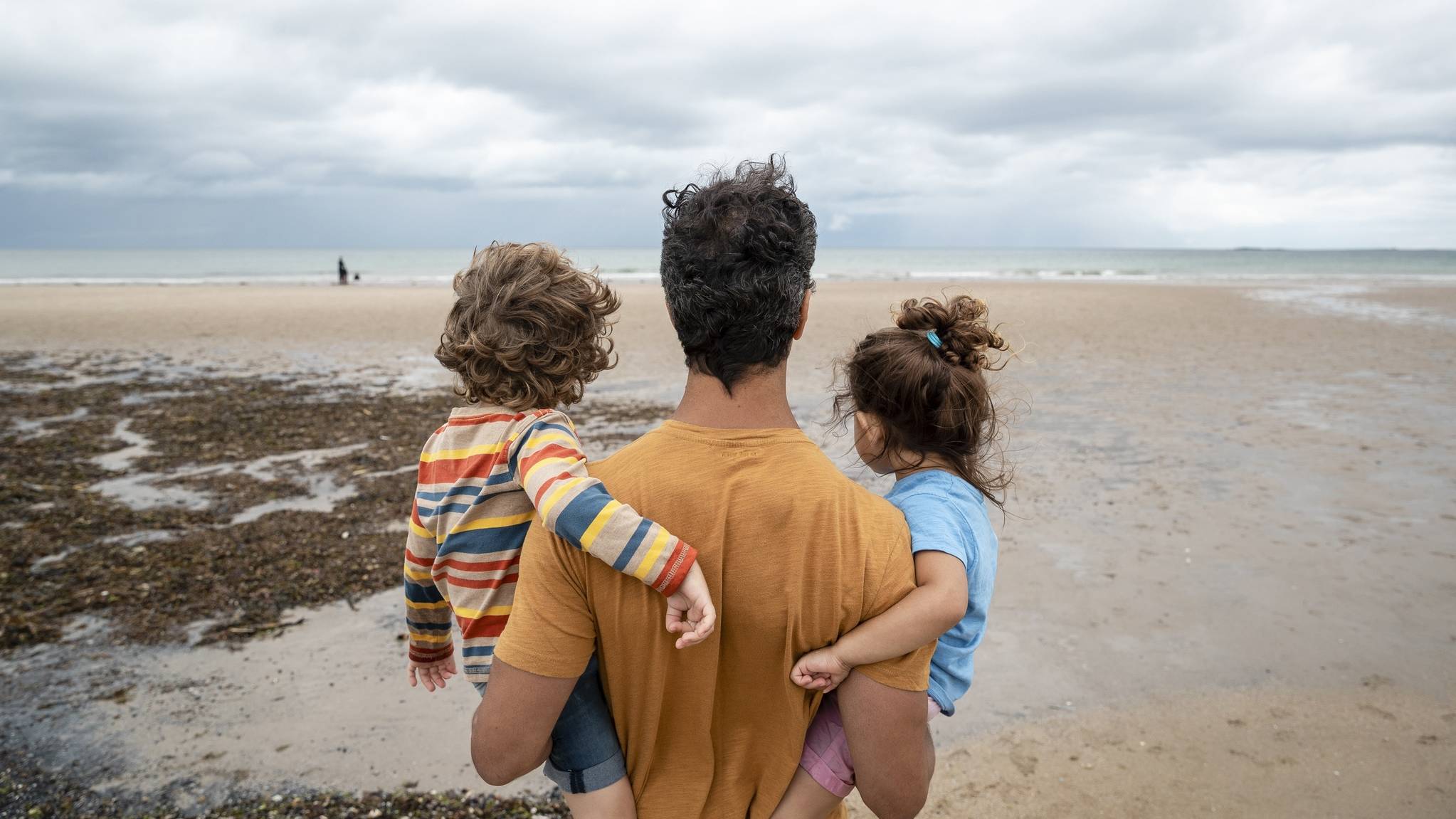 Parent carrying two children while looking out across a beach, symbolising financial security and future planning.