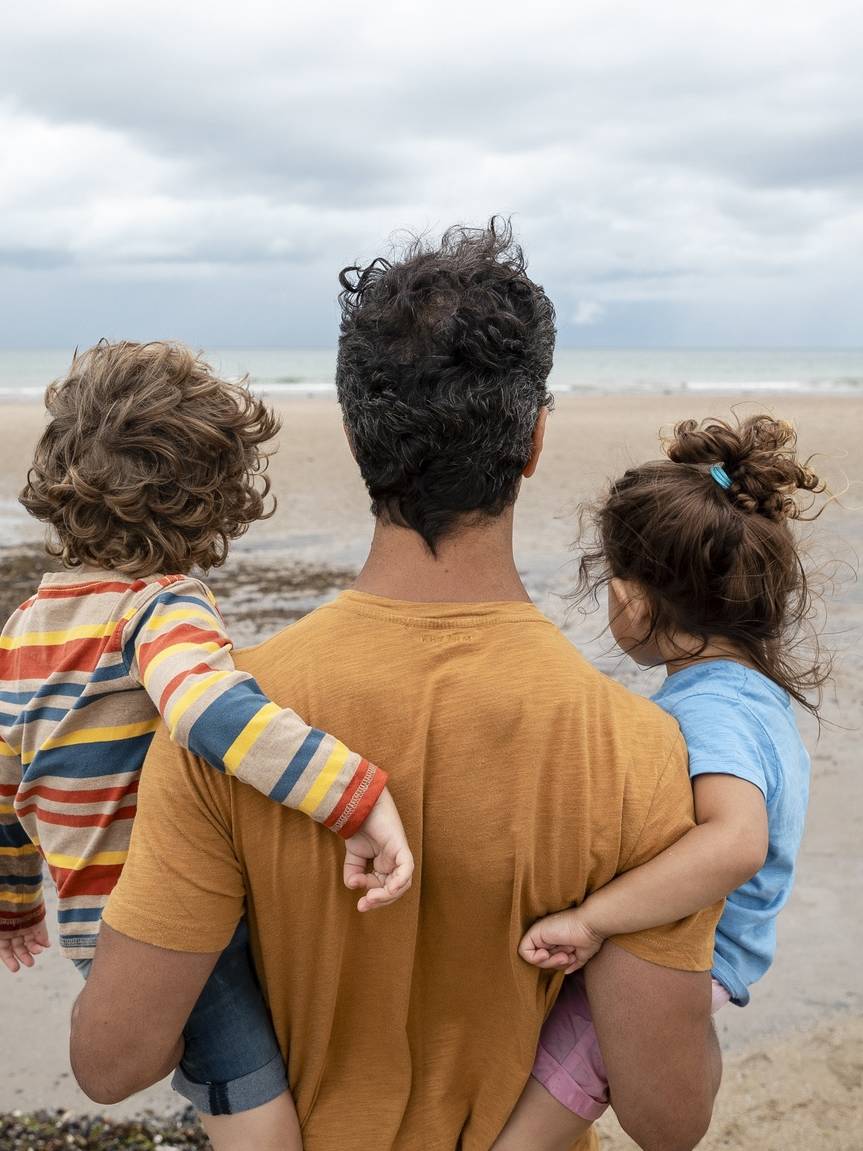 Parent carrying two children while looking out across a beach, symbolising financial security and future planning.
