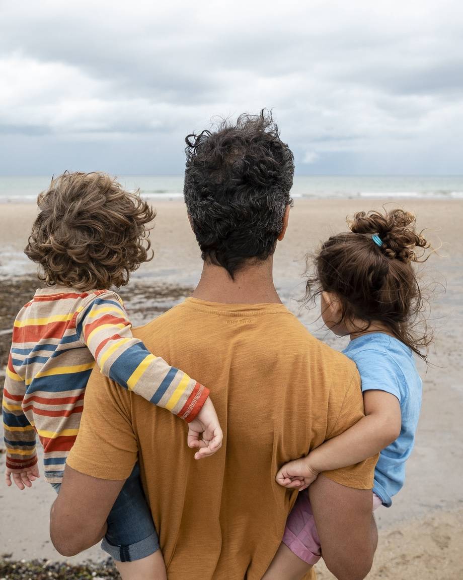 Parent carrying two children while looking out across a beach, symbolising financial security and future planning.
