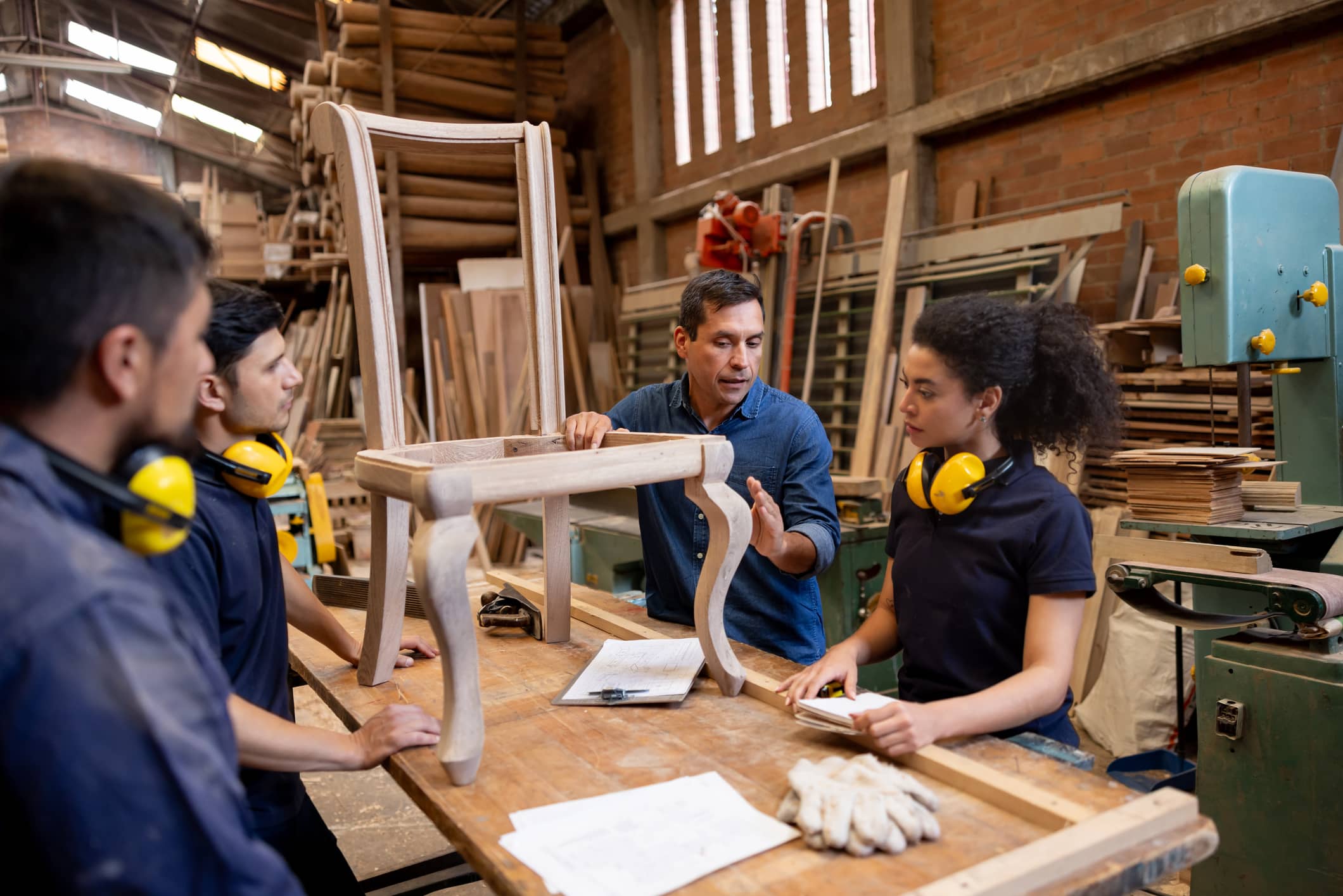 Experienced craft professional mentoring apprentices in a woodworking workshop as part of a phased retirement.