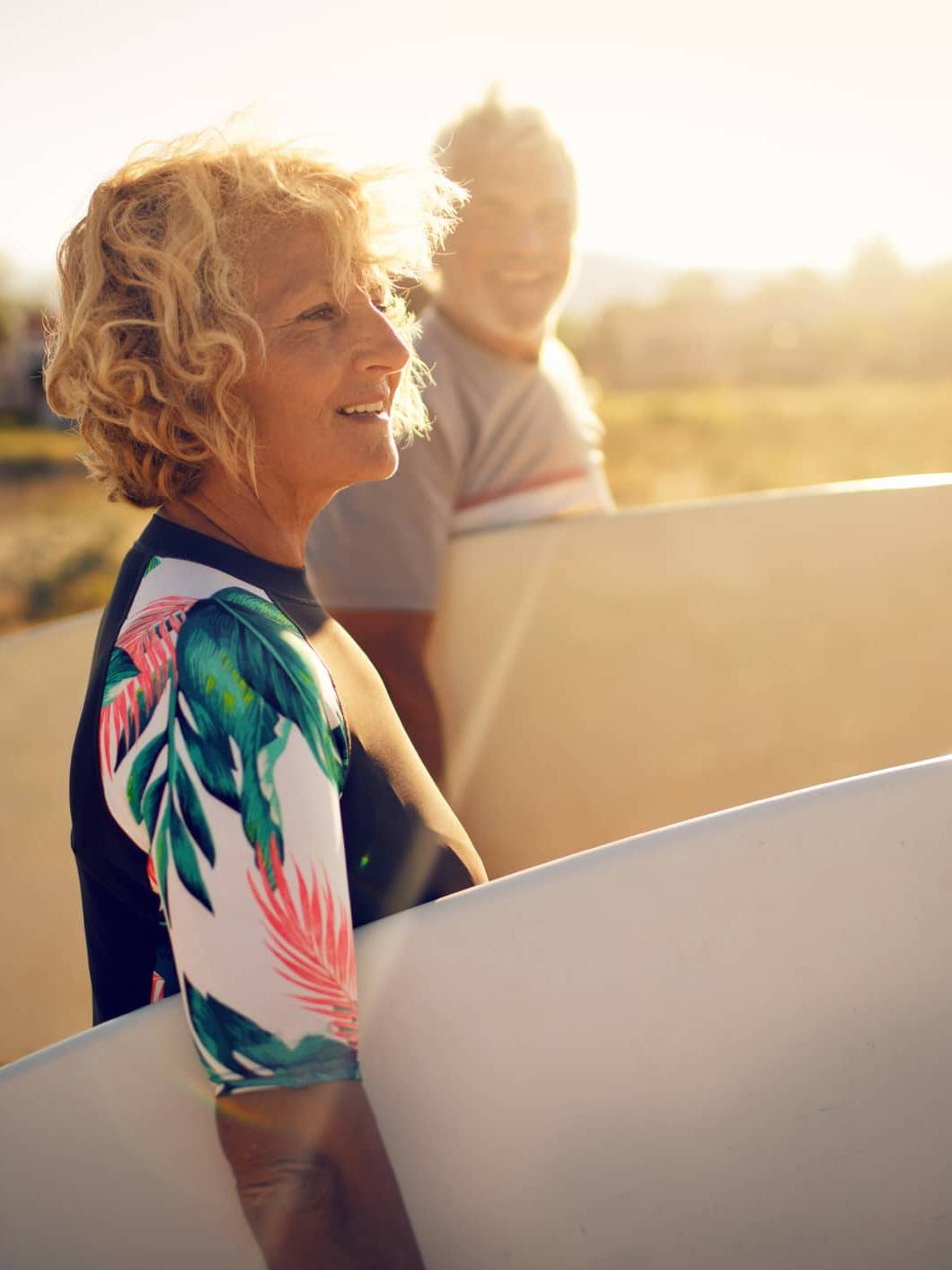Retired woman carrying a surfboard on the beach, symbolising financial confidence and retirement planning despite market volatility.