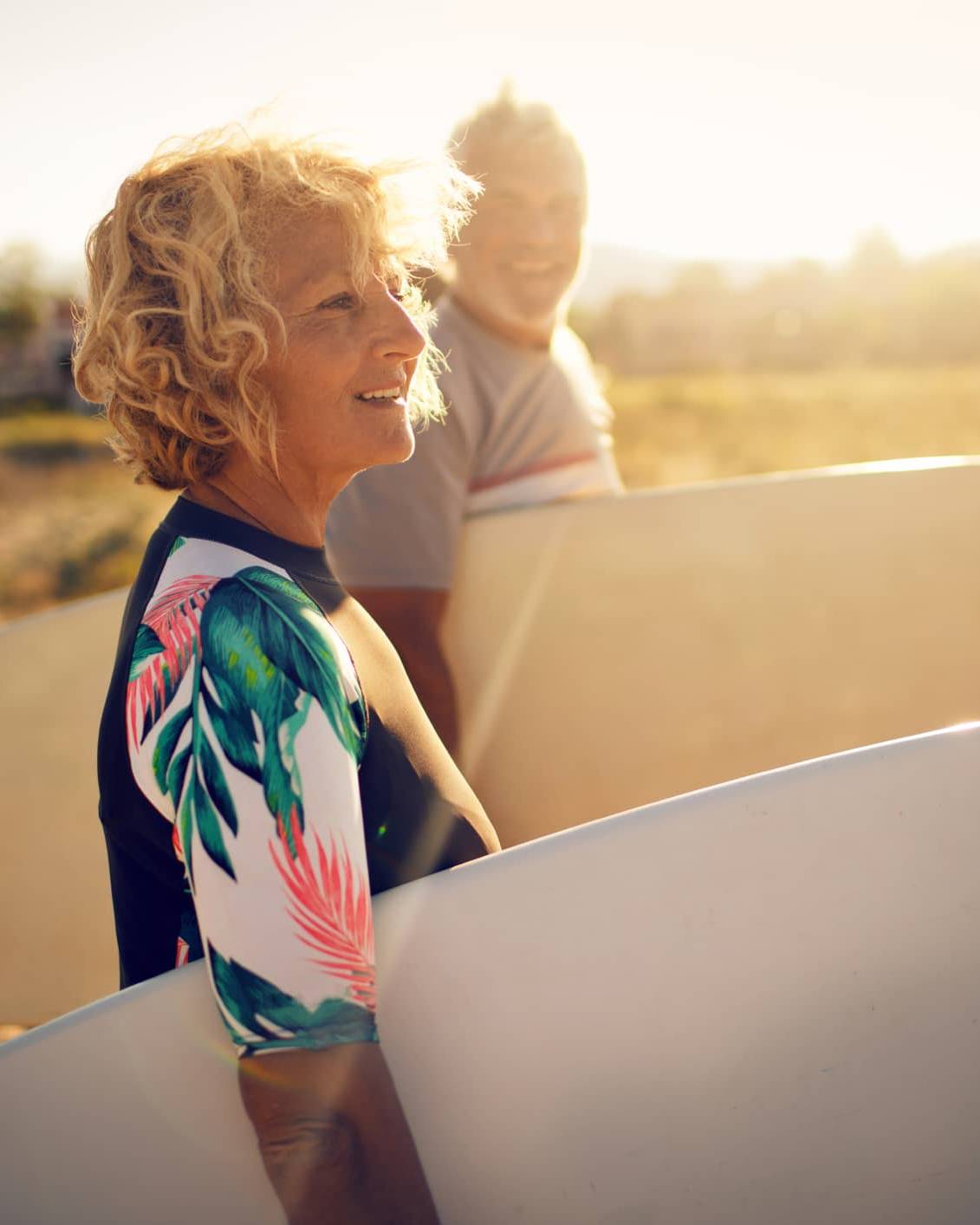 Retired woman carrying a surfboard on the beach, symbolising financial confidence and retirement planning despite market volatility.