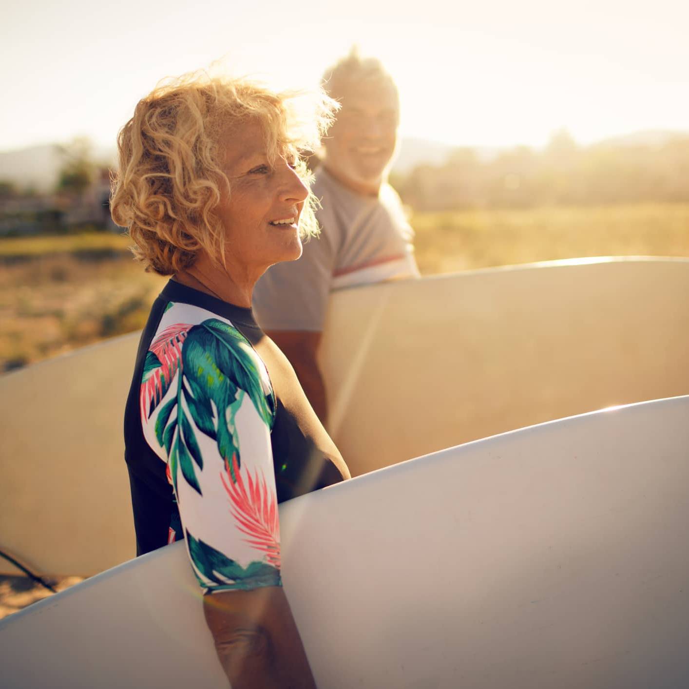 Retired woman carrying a surfboard on the beach, symbolising financial confidence and retirement planning despite market volatility.