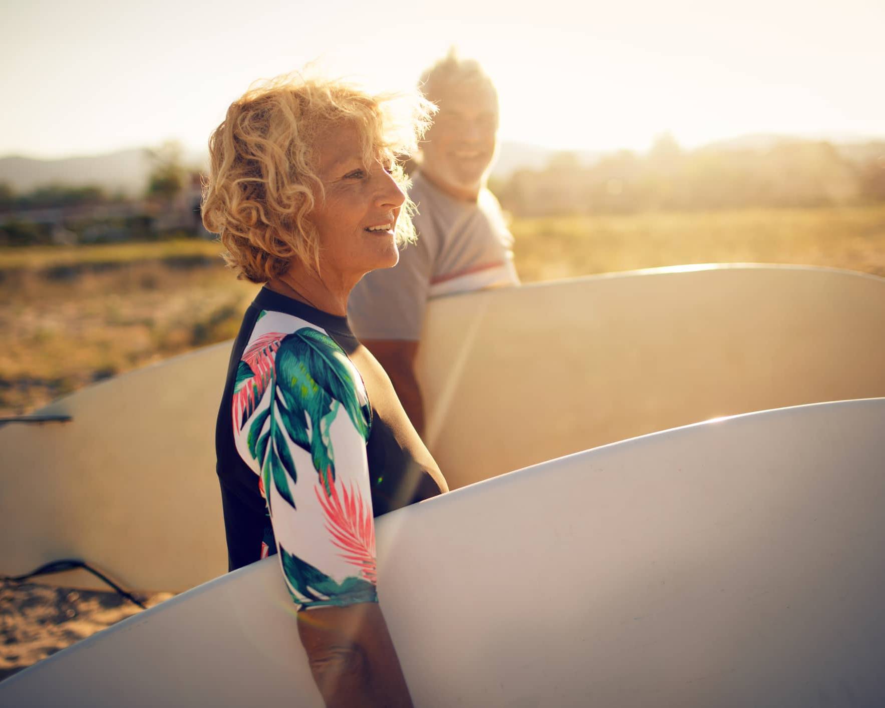 Retired woman carrying a surfboard on the beach, symbolising financial confidence and retirement planning despite market volatility.
