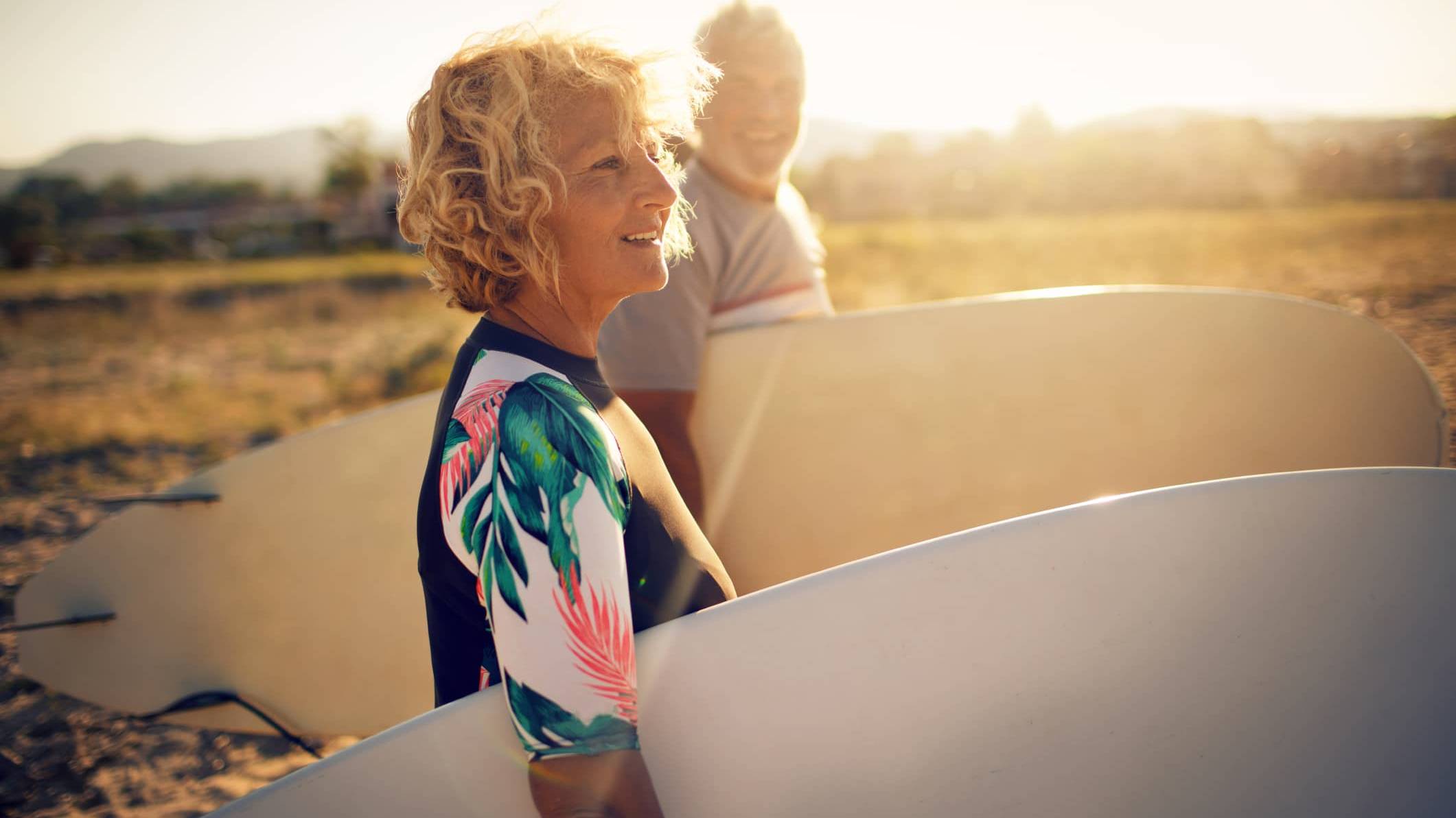 Retired woman carrying a surfboard on the beach, symbolising financial confidence and retirement planning despite market volatility.