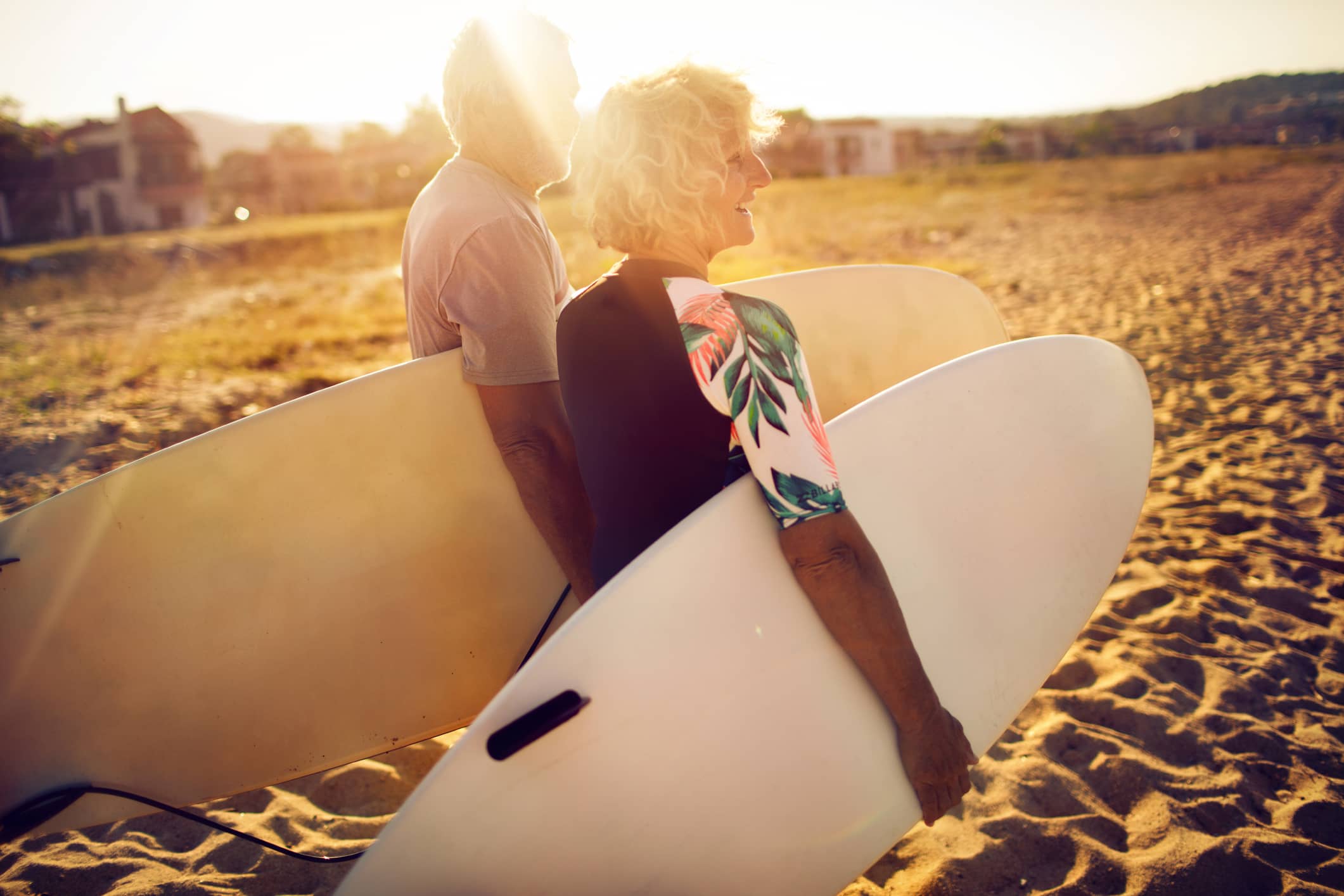 Active retired couple carrying surfboards on the beach after retirement, representing retirement planning and financial security.