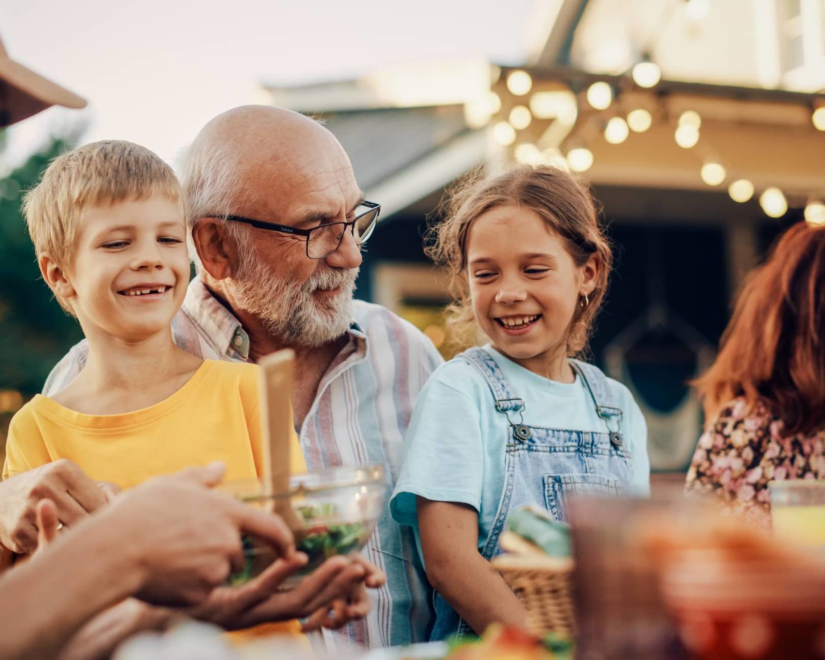 Three generations of a family enjoying a meal together outdoors, representing legacy planning and passing wealth between generations.