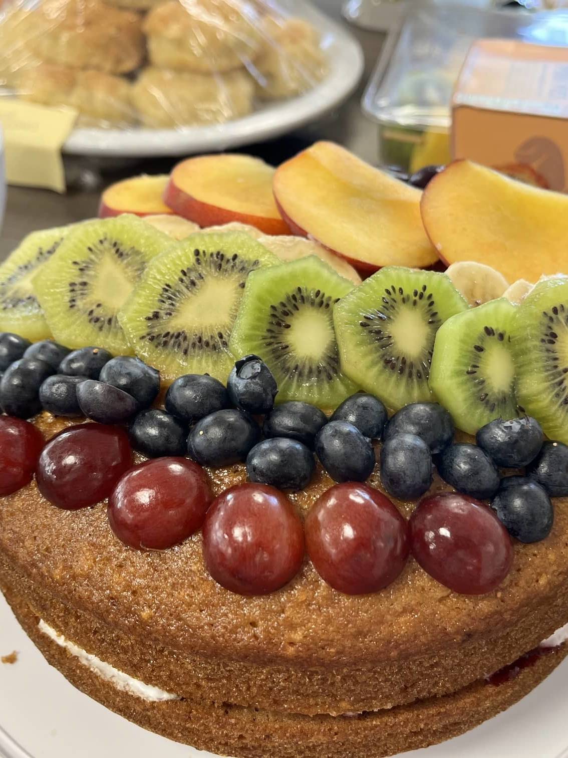 Fresh fruit-topped Victoria sponge cake prepared for Amber River East Anglia's Pride Month charity bake sale.