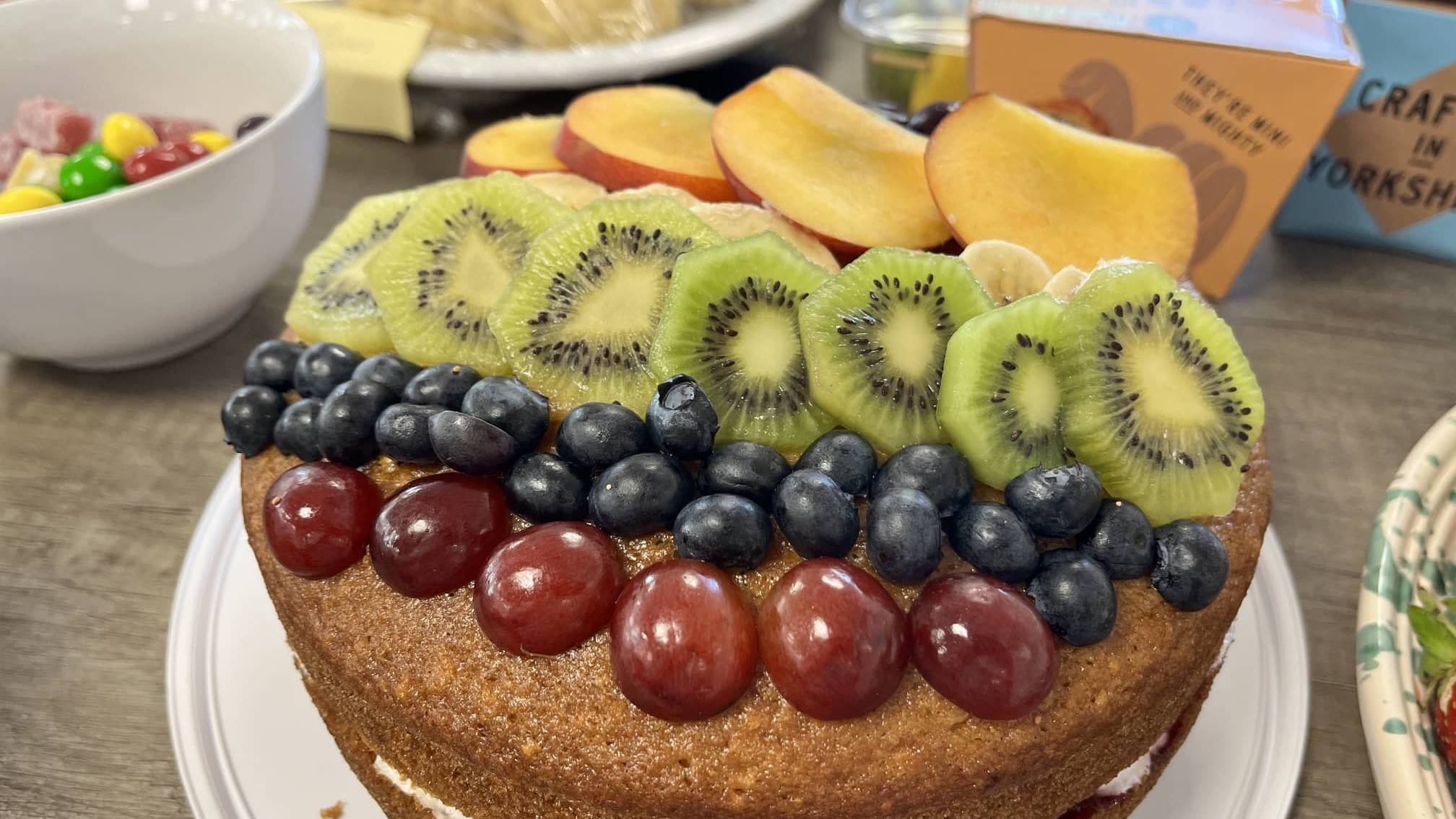 Fresh fruit-topped Victoria sponge cake prepared for Amber River East Anglia's Pride Month charity bake sale.
