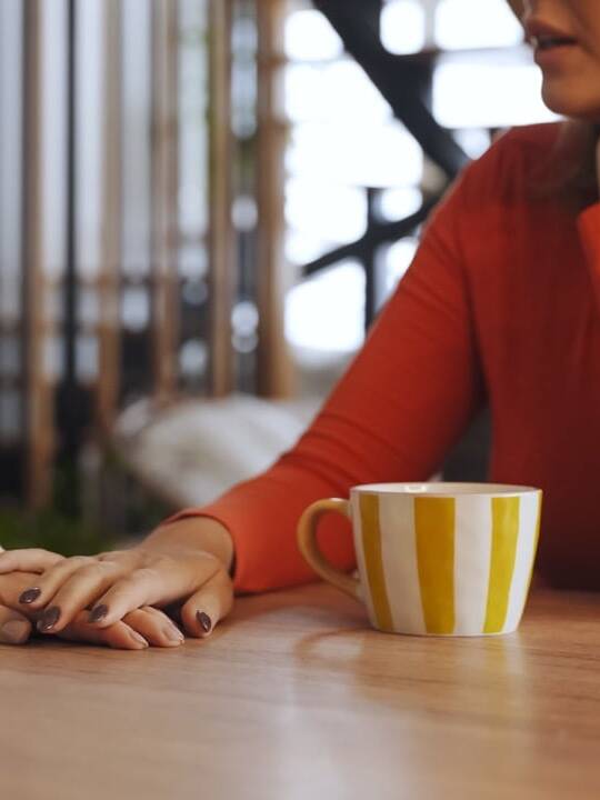 Mature woman talking with another person over coffee at a kitchen table
