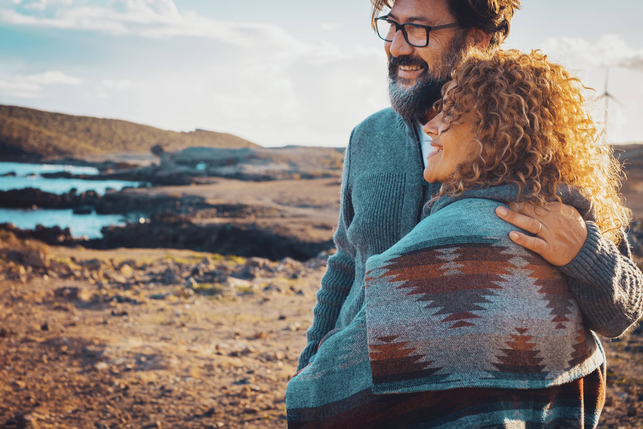 Couple in their 50s embracing beside a coastal landscape
